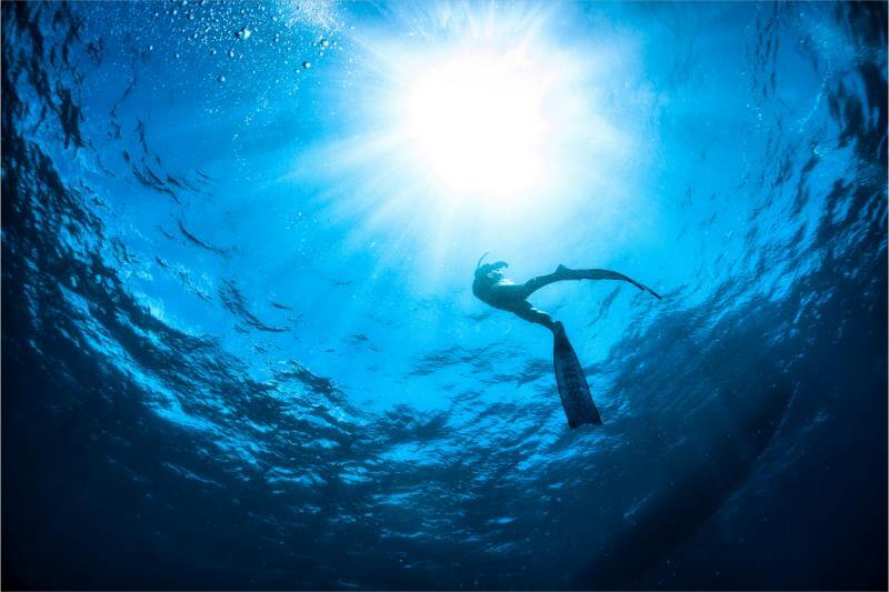 日のさす海の中を泳ぐダイバー